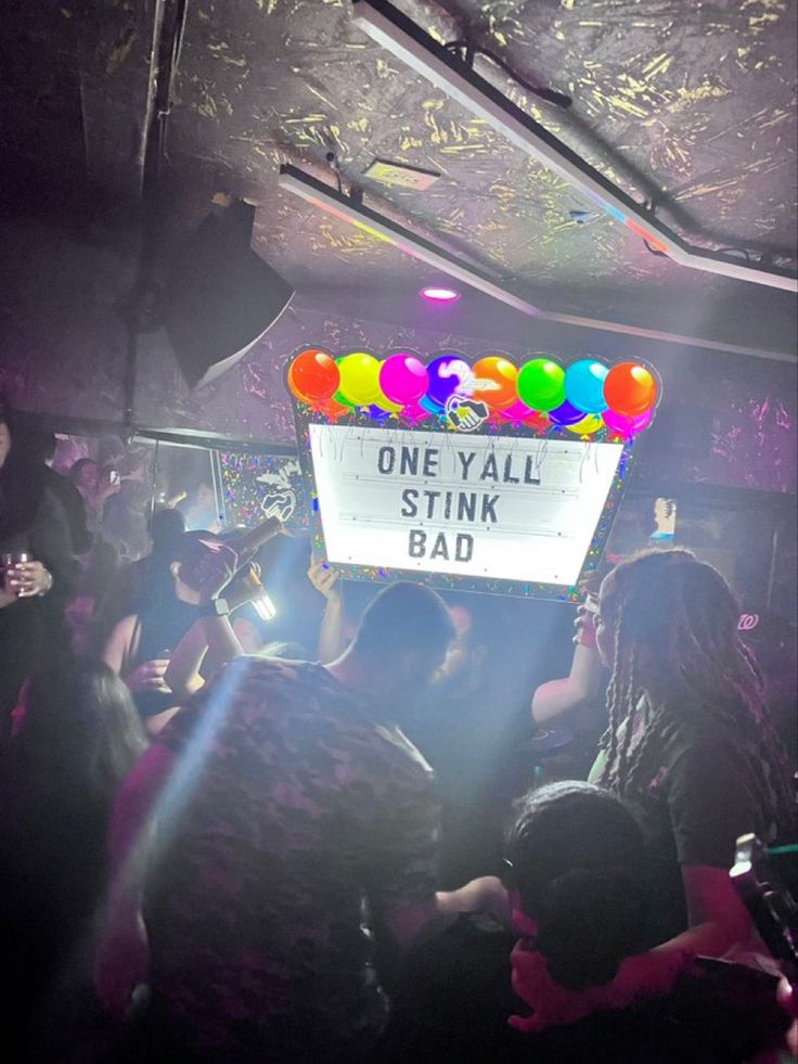 a sign that says one y'all stink bad surrounded by people in a club