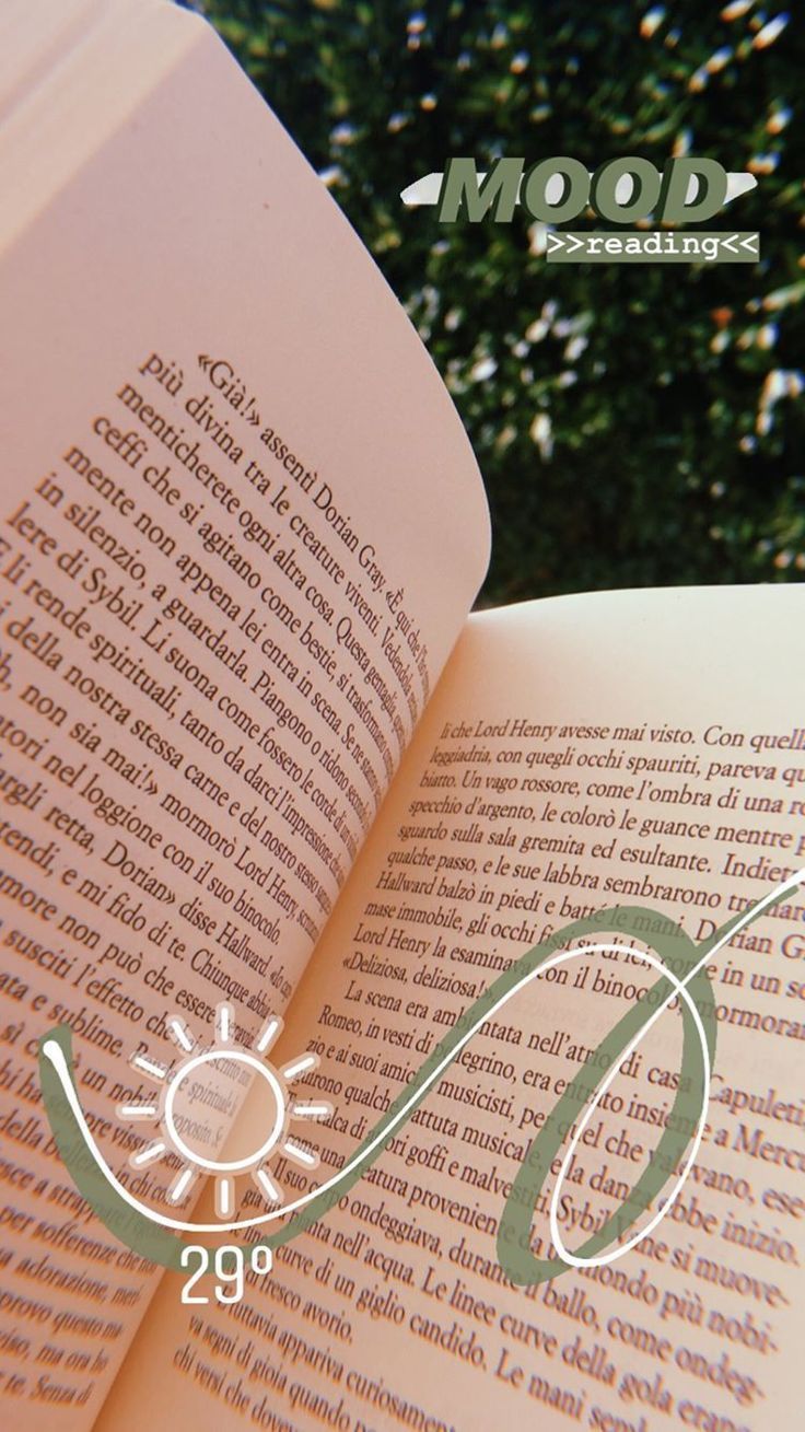 an open book sitting on top of a wooden table next to a tree and bushes