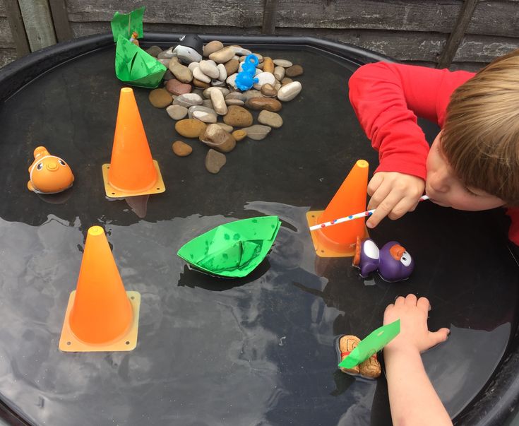 a young boy is playing with toys in an outdoor water play area that includes plastic cones and boats