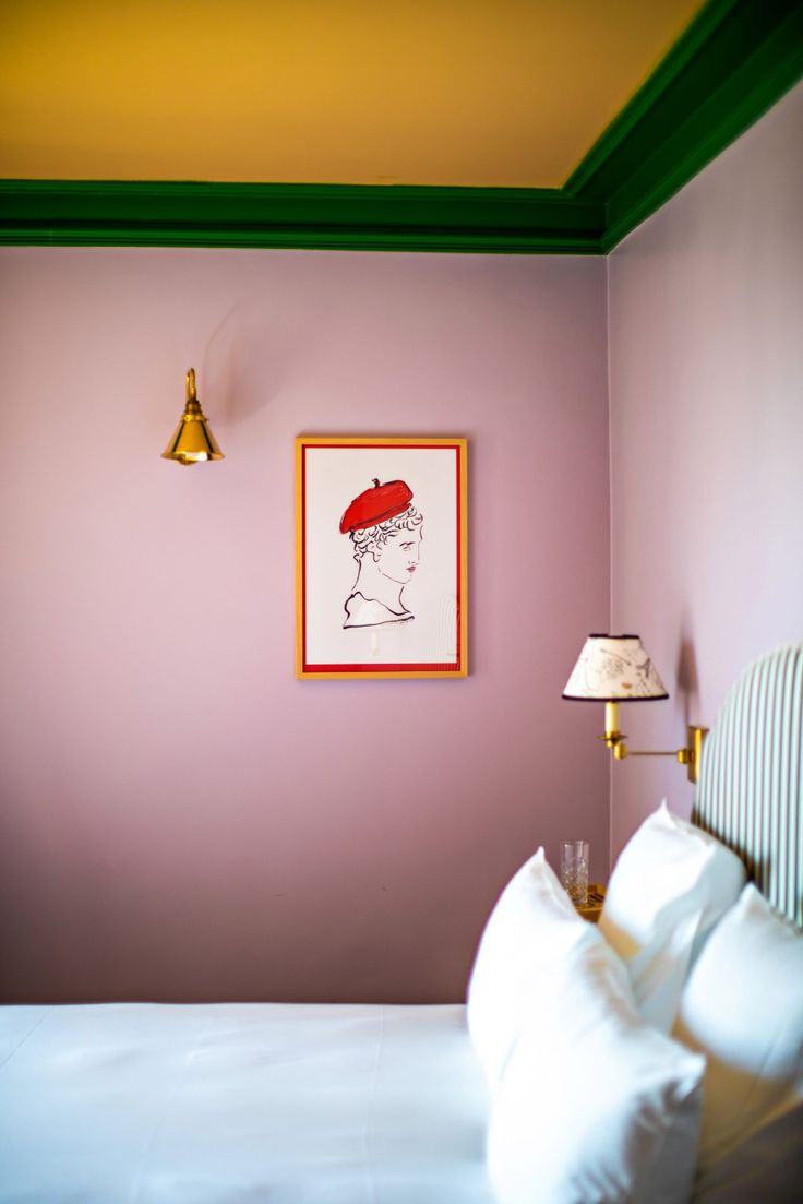 a bedroom with pink walls and green trim on the headboard, white bedding, and framed artwork