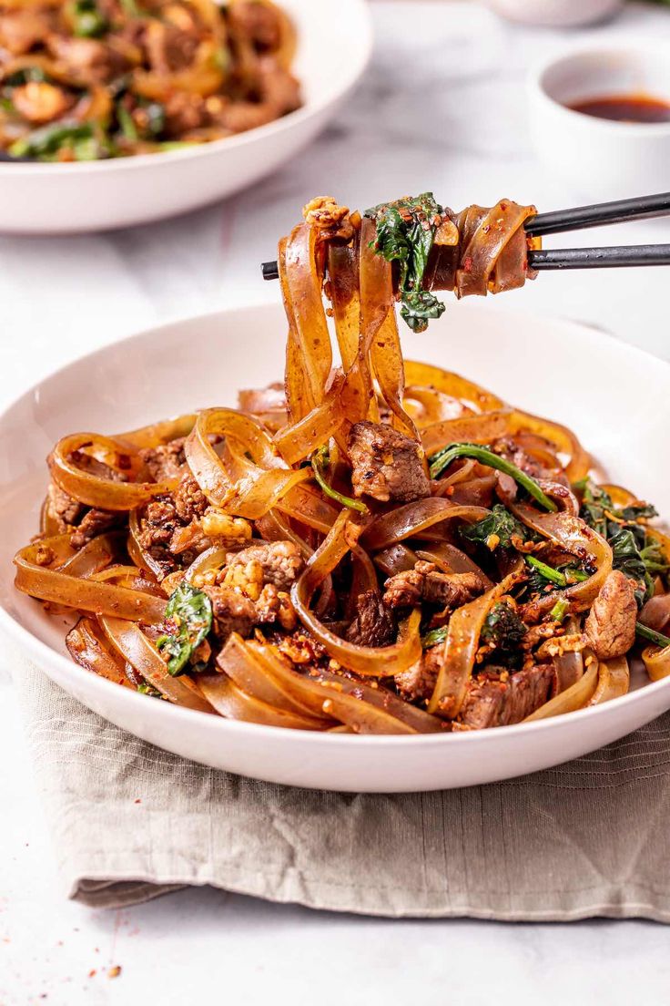 someone is holding chopsticks over a bowl of noodles with meat and spinach