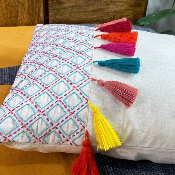 a white pillow with multicolored tassels sitting on top of a wooden table