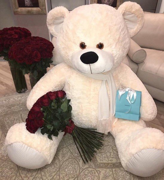 a large white teddy bear sitting on top of a couch next to flowers and a bag