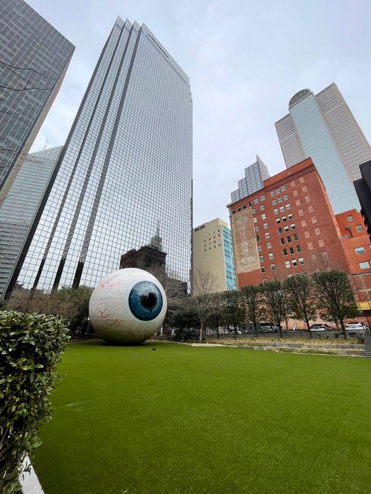 an artificial eyeball sits in the middle of a grassy area between two tall buildings