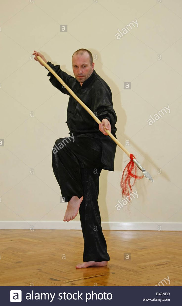 a man in black clothes holding a broom and standing on one leg with his legs spread out