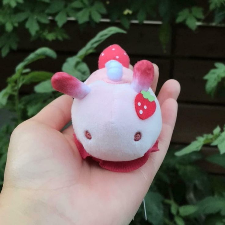 a hand holding a small stuffed animal with a strawberry on it's head and ears