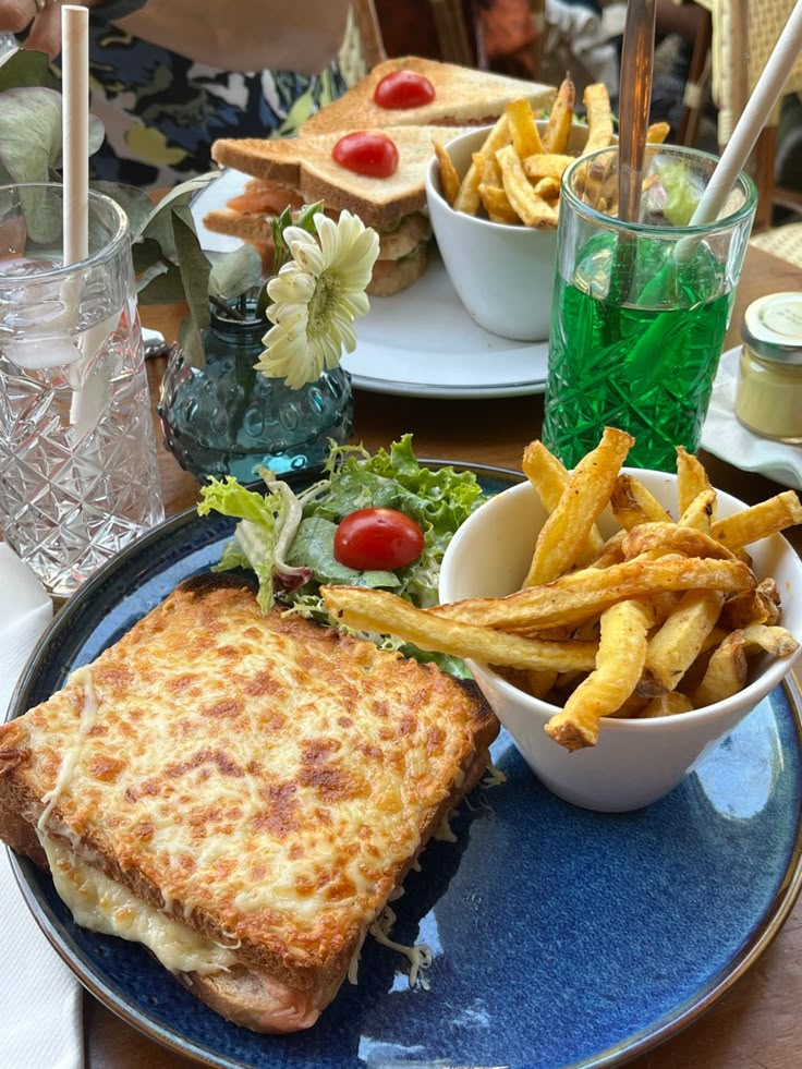 a blue plate topped with a sandwich and french fries next to a bowl of salad