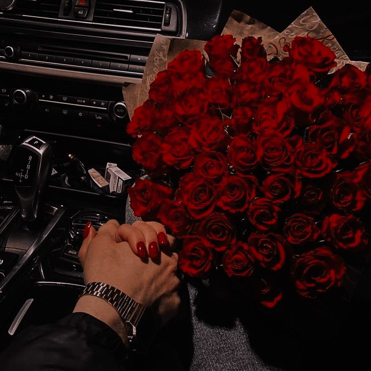 a woman is holding a bouquet of red roses in her hand while sitting next to the car