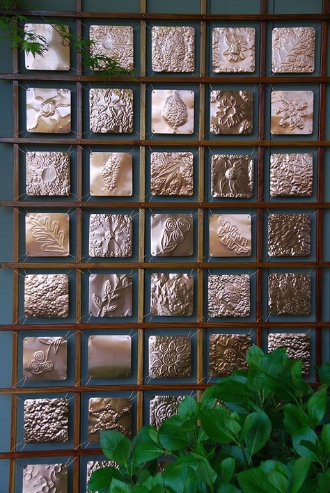 a potted plant sitting in front of a wall covered with metal squares and leaves