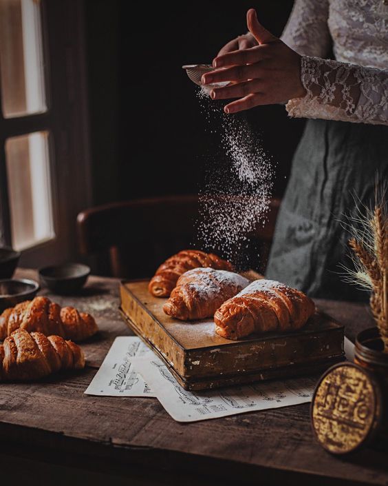 a person sprinkling sugar on some croissants