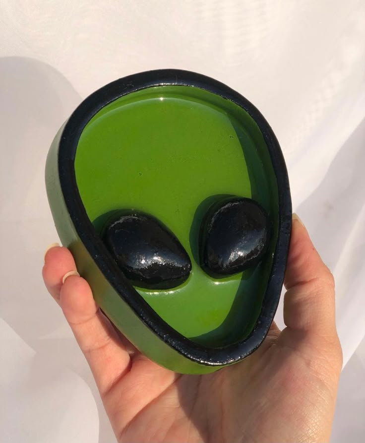 a hand holding a green and black alien bowl