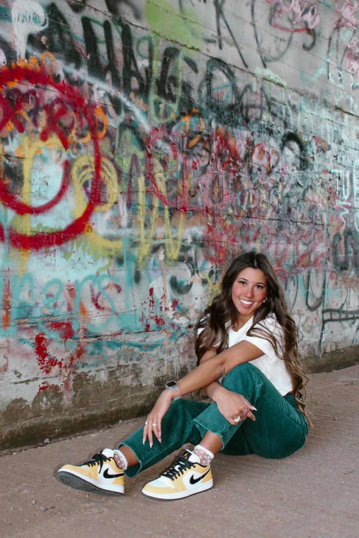 a woman sitting on the ground in front of graffiti covered wall