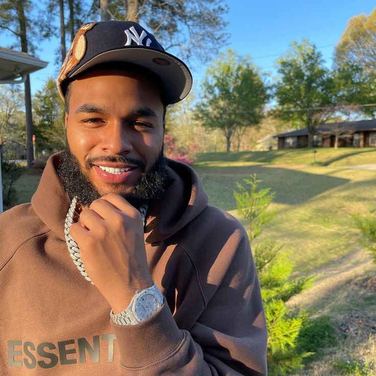 a man with a beard wearing a baseball cap and hoodie smiling at the camera