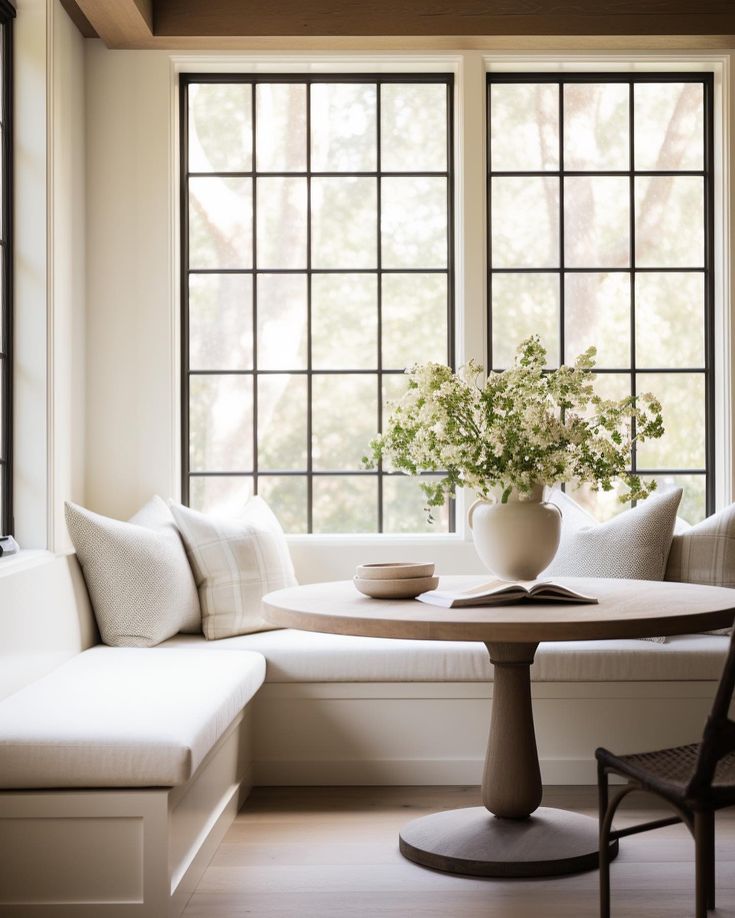 a white couch sitting next to a table in a living room under two large windows