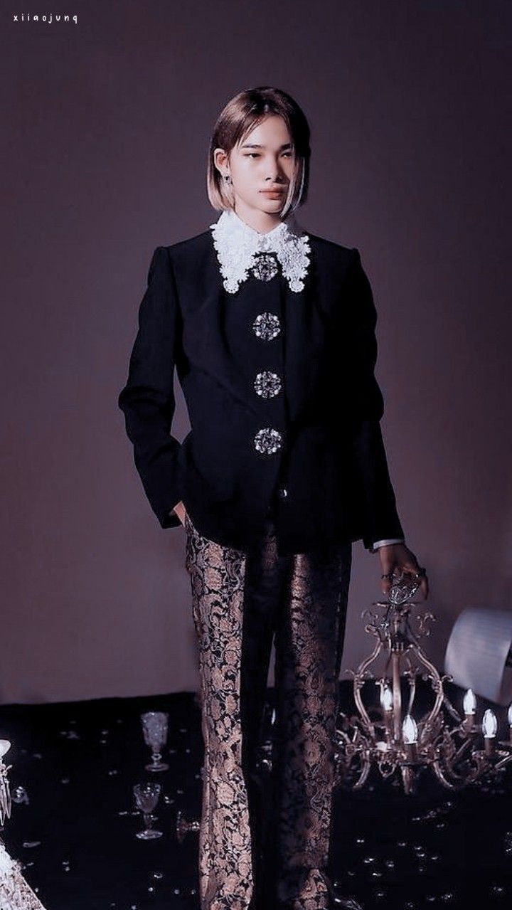 a woman standing in front of a chandelier wearing black and gold pants with white lace