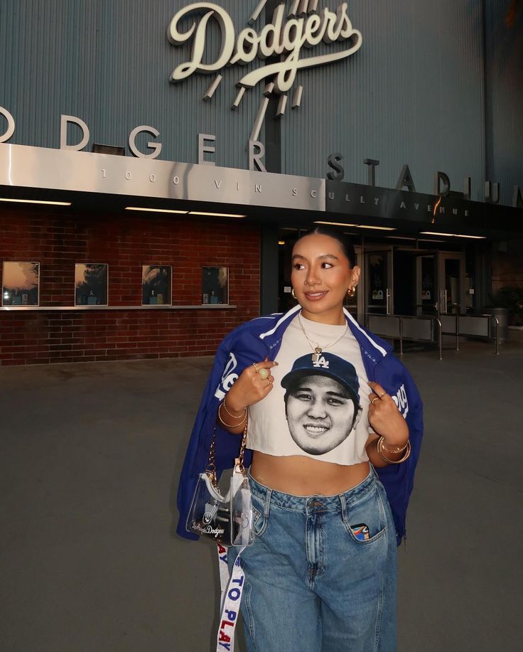 a woman standing in front of dodger stadium holding onto her t - shirt with the dodgers logo on it