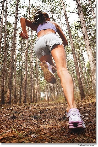 a woman is running through the woods with her feet in the air while wearing shorts