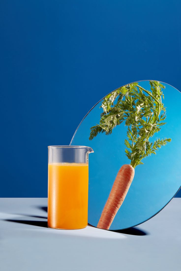 an orange juice in a glass next to a plate with a carrot on it and a blue background