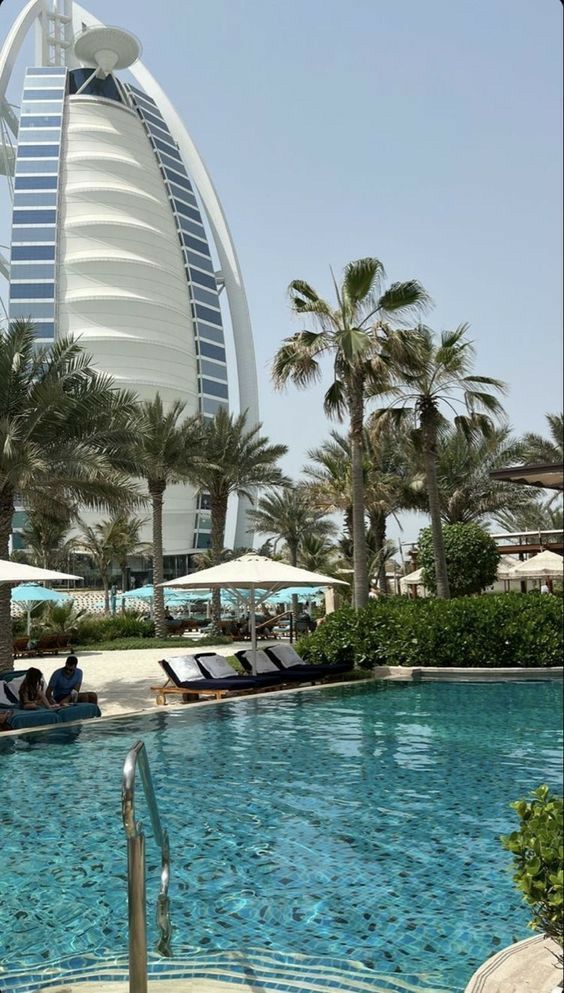 an outdoor swimming pool with lounge chairs and umbrellas in front of the burj