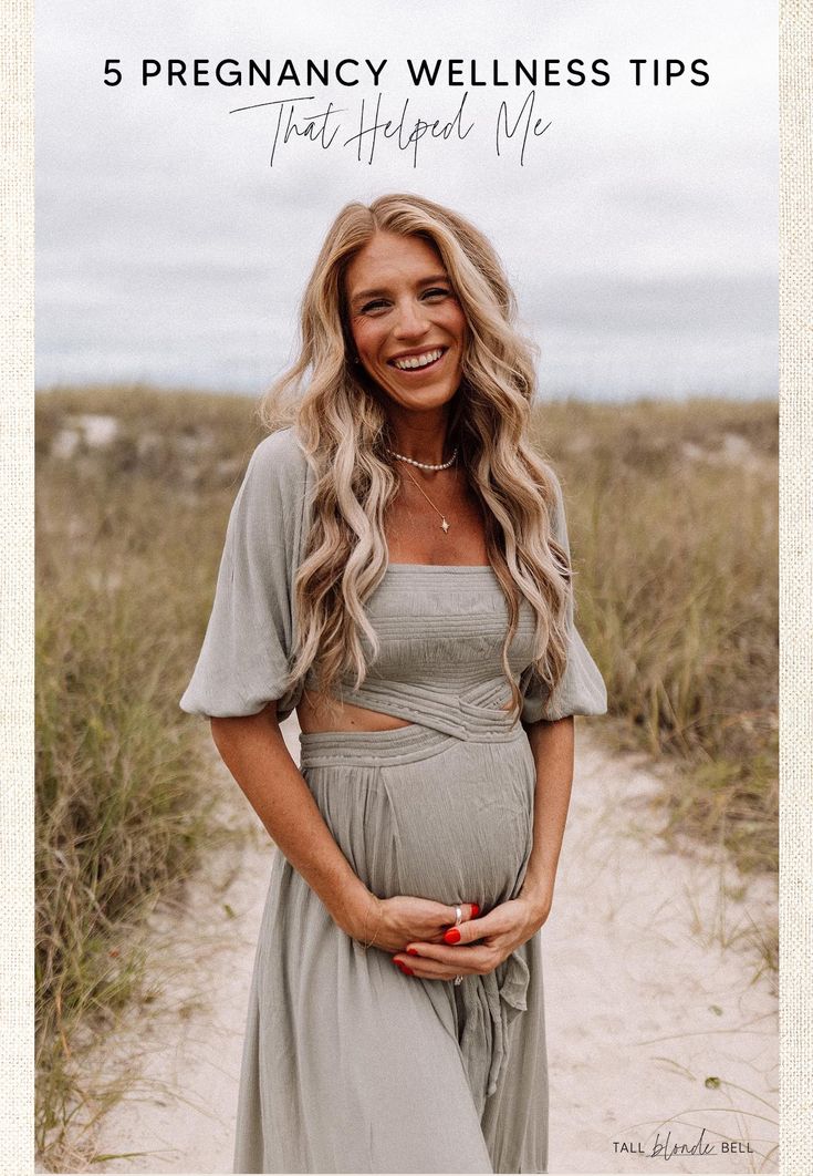 a pregnant woman standing in the sand with her belly exposed and smiling at the camera