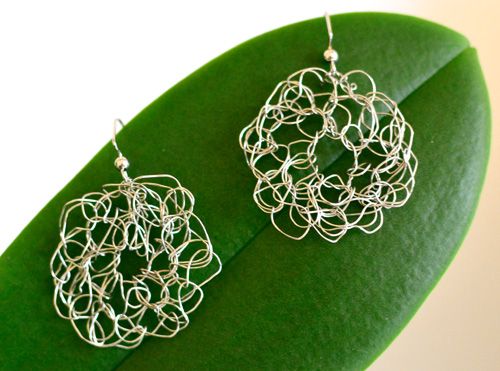 two silver earrings sitting on top of a green leaf