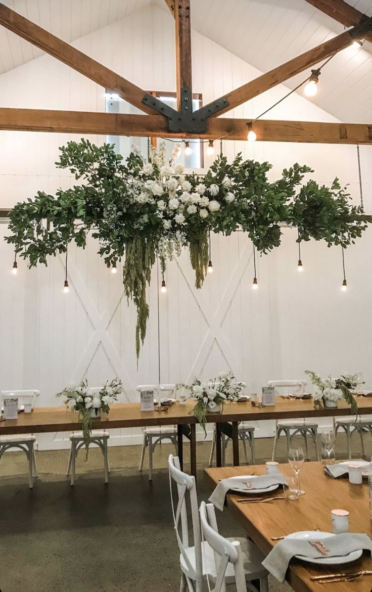 the tables are set with white flowers and greenery hanging from the ceiling above them