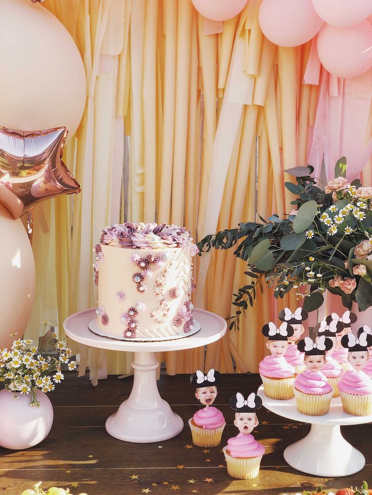 there is a cake and cupcakes on the table with balloons in the background