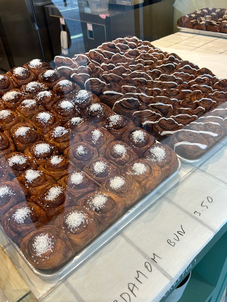 two trays of pastries on display in a pastry shop, one with chocolate and the other topped with powdered sugar