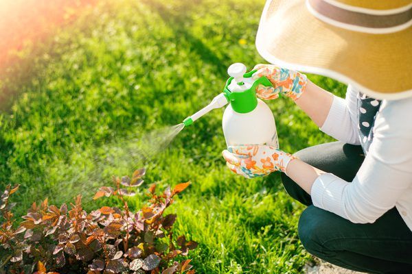 a woman in a hat is spraying water on her hands with a garden hose and sprinkler