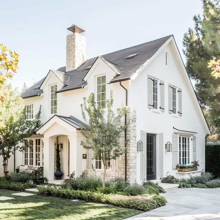 a white house with lots of windows and bushes around it's front lawn area