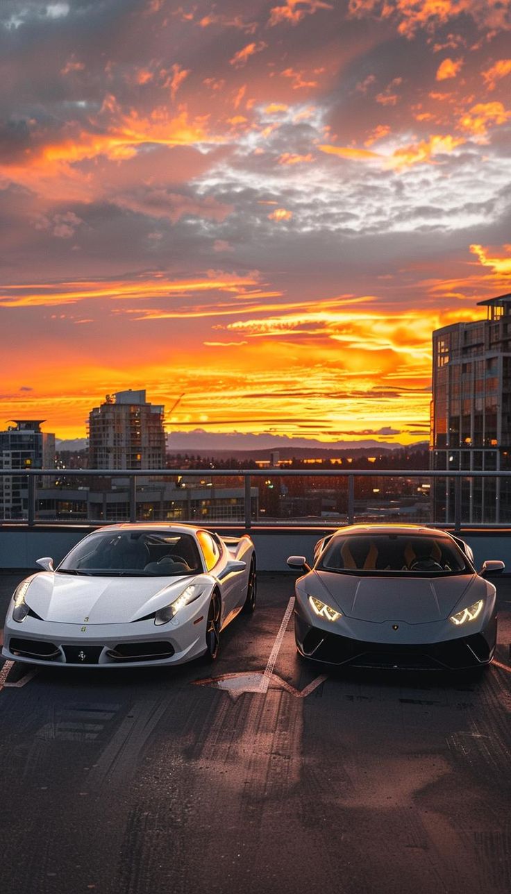 two white sports cars parked next to each other in front of a city skyline at sunset