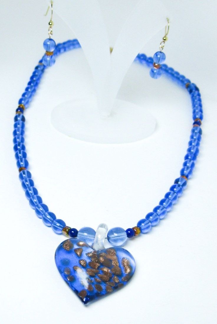 Blue glass heart-shaped pendant with gold random shapes (Austin Hamilton) on cornflower blue glass round bead necklace earring set 14K gold-filled. 18-inch glass necklace glass heart pendant earring set 14K gold-filled. The round cornflower blue beads are 6 mm. The gold tone cylindrical rondelles are 3 x 3 mm. There are four 4mm lapis beads in the necklace. The 14K gold-filed lobster clasp is 11 mm.  The heart shaped pendant is 1.2 inches wide x 1.2 inches long.  The earrings are on 14K gold-filled earwires and have a 0.6-inch drop. Single Strand Heart Shaped Jewelry For Gifts, Glass Single Strand Jewelry Gift, Luxury Single Strand Glass Jewelry For Gift, Blue Heart Beads Necklace As Gift, Elegant Blue Jewelry With Heart Beads, Blue Czech Glass Jewelry For Gifts, Blue Necklace With Round Heart Charm, Blue Necklace With Heart Charm, Blue Necklaces With Heart Charm And Round Shape