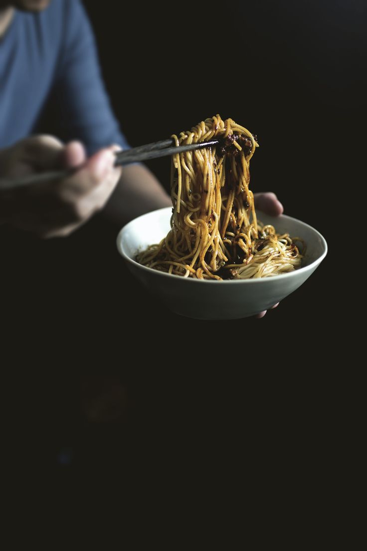 a person holding a bowl of noodles with chopsticks in their hands, while eating it