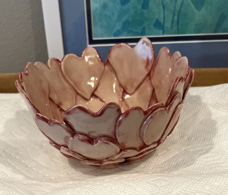 a pink and white bowl sitting on top of a table next to a framed painting