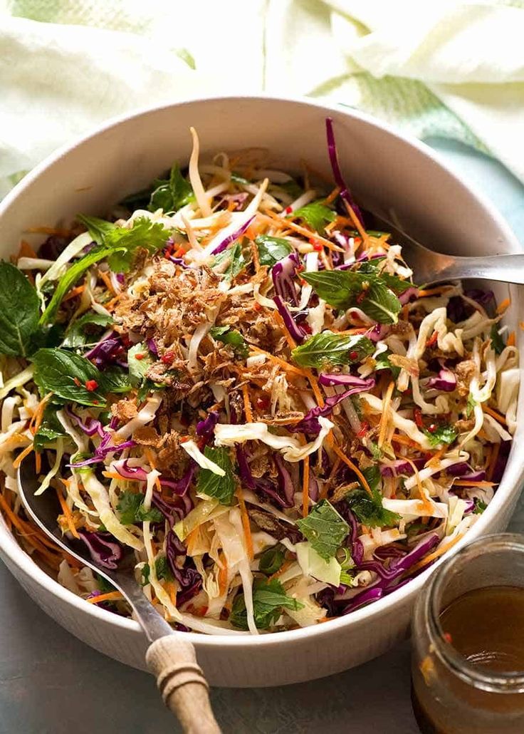 a white bowl filled with coleslaw and carrots next to a jar of dressing