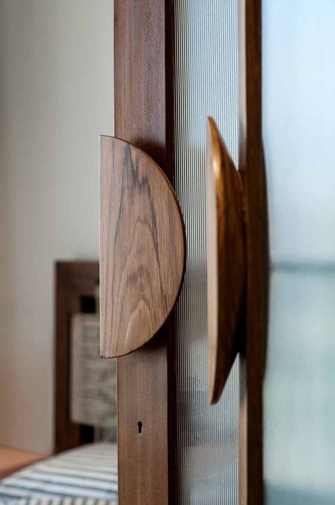 a close up of a wooden door handle on a glass door with a bed in the background