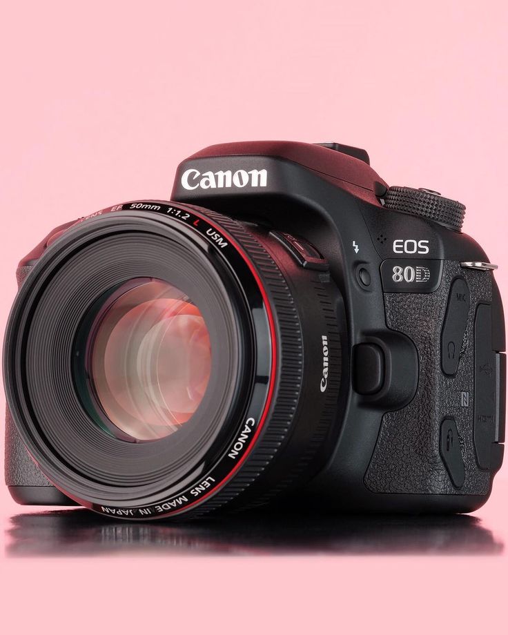 a canon camera sitting on top of a pink surface with the lens up close to it's body