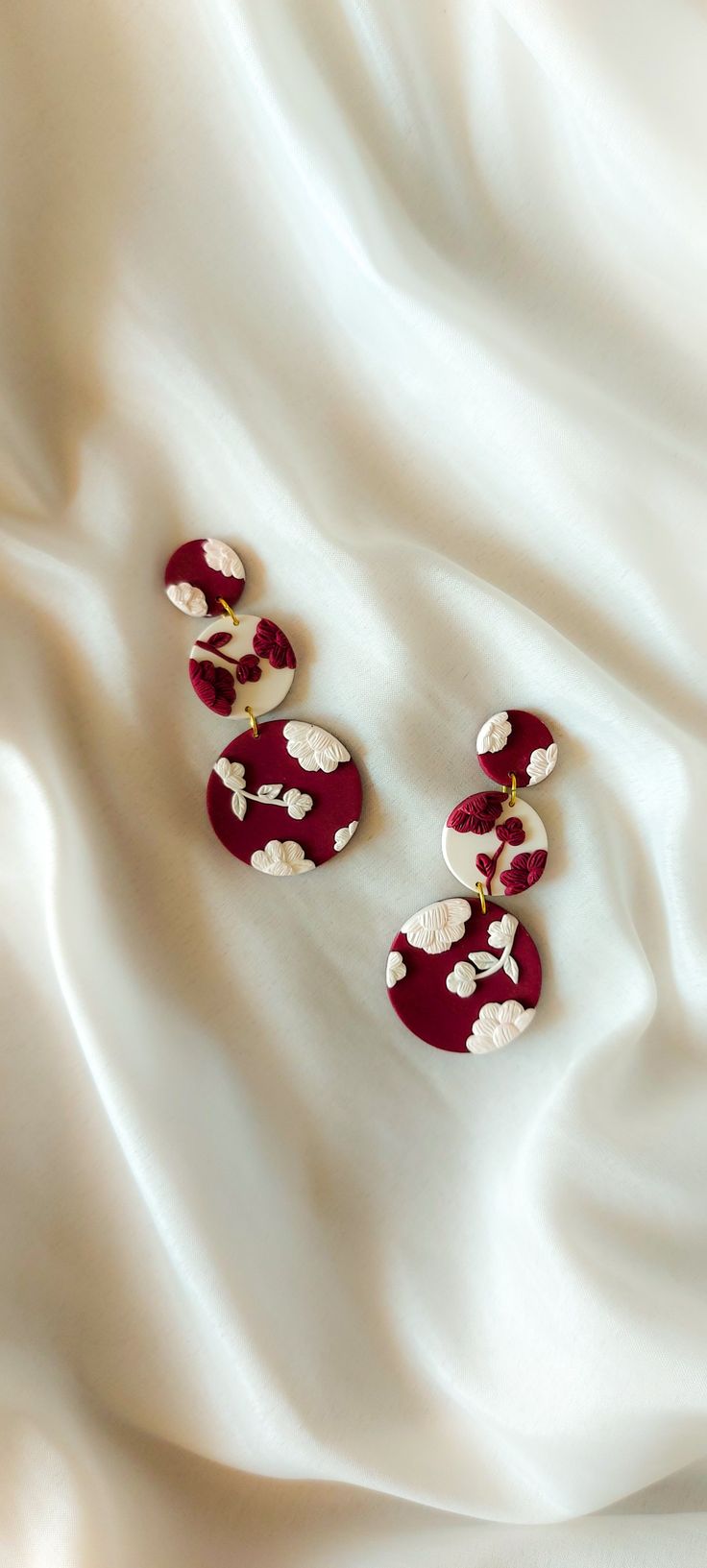 two pairs of red and white earrings sitting on top of a white cloth