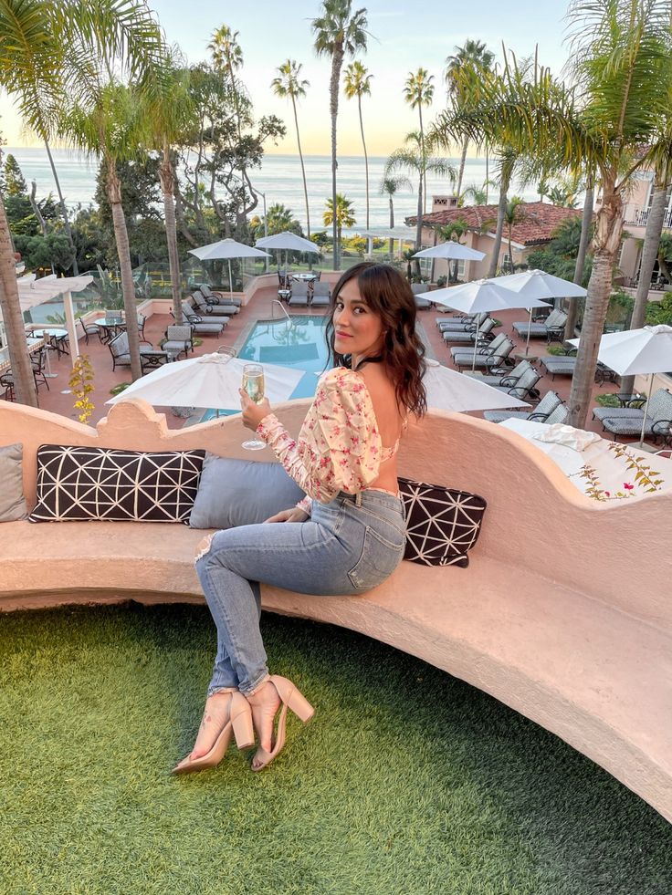 a woman sitting on top of a wooden bench next to a lush green field with palm trees