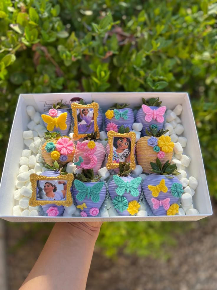 a person holding up a tray with decorated cookies in the shape of flowers and frames