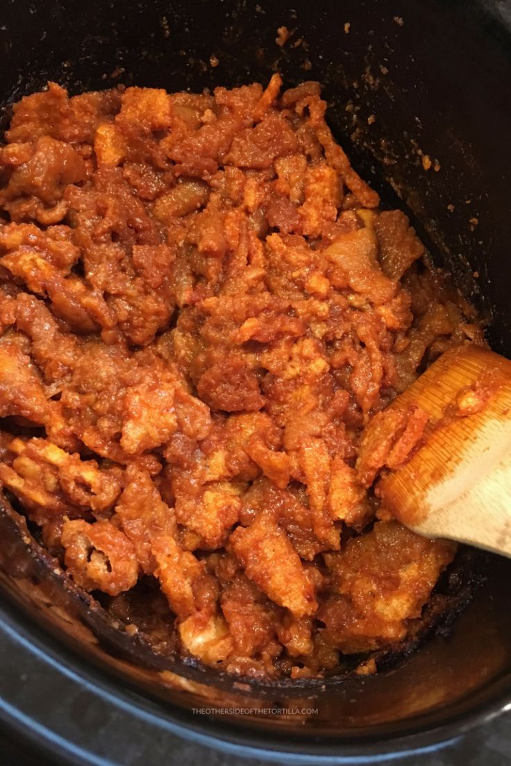 the food is being cooked in the crock pot with a wooden spatula next to it