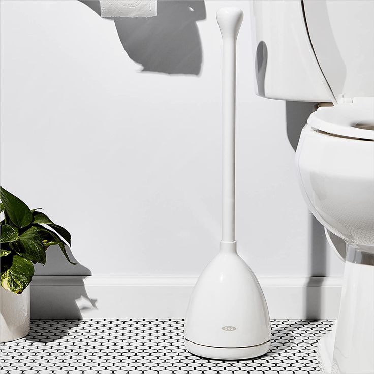 a white toilet sitting next to a potted plant on top of a tiled floor