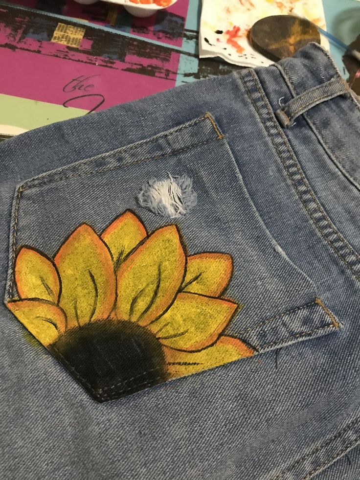 a sunflower painted on the back of a pair of jeans with spoons nearby