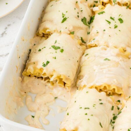 a white casserole dish filled with pasta and meat covered in cheese sauce, garnished with parsley