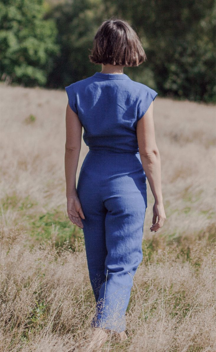 a woman in blue jumpsuit walking through tall grass