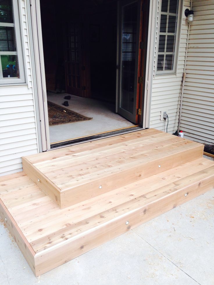 a wooden deck with steps leading to the front door and an open patio door behind it