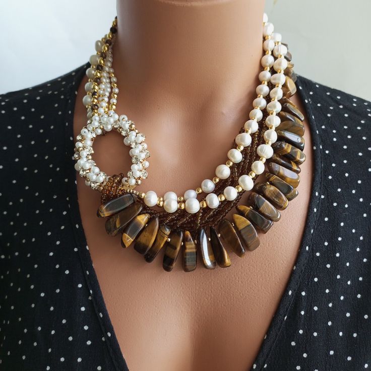 Meet our stunning Pearl and Tiger Eye Beaded Necklace! This elegant piece is a true reflection of elegance and style. Crafted with meticulous precision, this necklace features vibrant Tiger Eye beads that contrast beautifully with the Pearl beads. The combination of these rich gemstones creates a striking and eye-catching design. Each bead has been carefully selected for its unique color and texture, making this necklace a truly one-of-a-kind accessory. MATERIALS:Baroque Pearl Beads. Brown Tiger Large Bead Necklace Ideas, Handmade Beaded Necklaces Design, Tiger Eye Necklace, Brown Tiger, Long Statement Necklace, Tigers Eye Necklace, Beaded Necklace Diy, Natural Stone Jewelry, Tiger Eye Beads