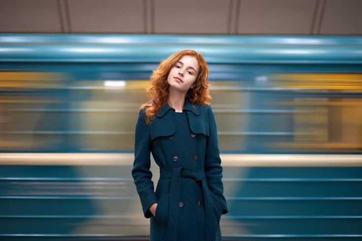 a woman with red hair standing in front of a train and looking at the camera