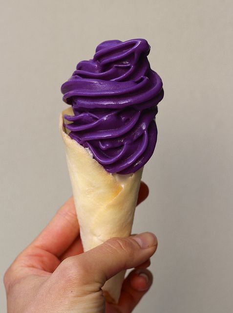 a hand holding an ice cream cone with purple icing