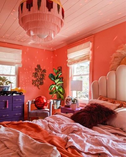 a bedroom with pink walls and orange bedding in the center is decorated with potted plants